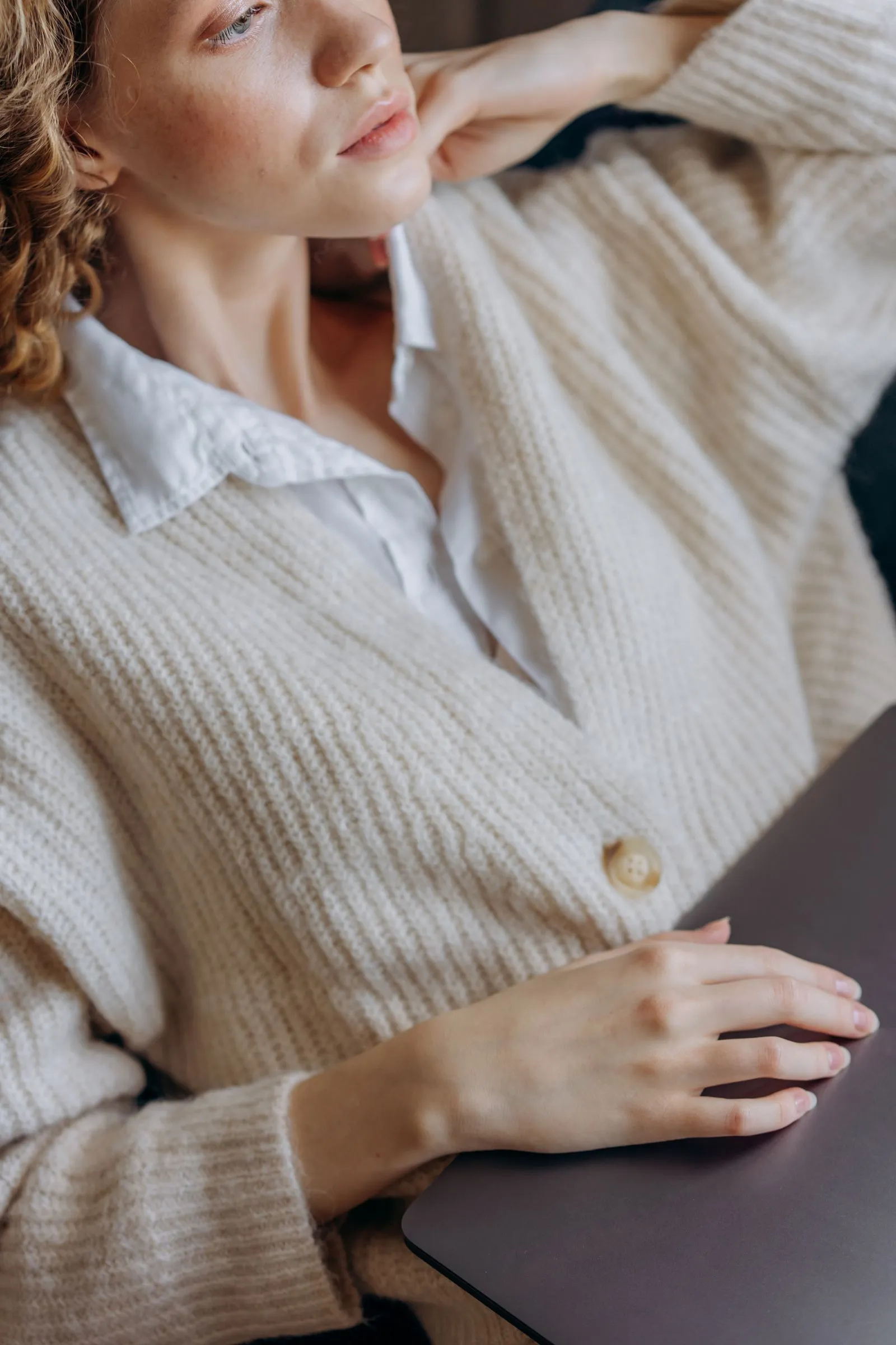 A person relaxed in a soft cream organic-cotton cardigan over a white shirt, in warm natural light