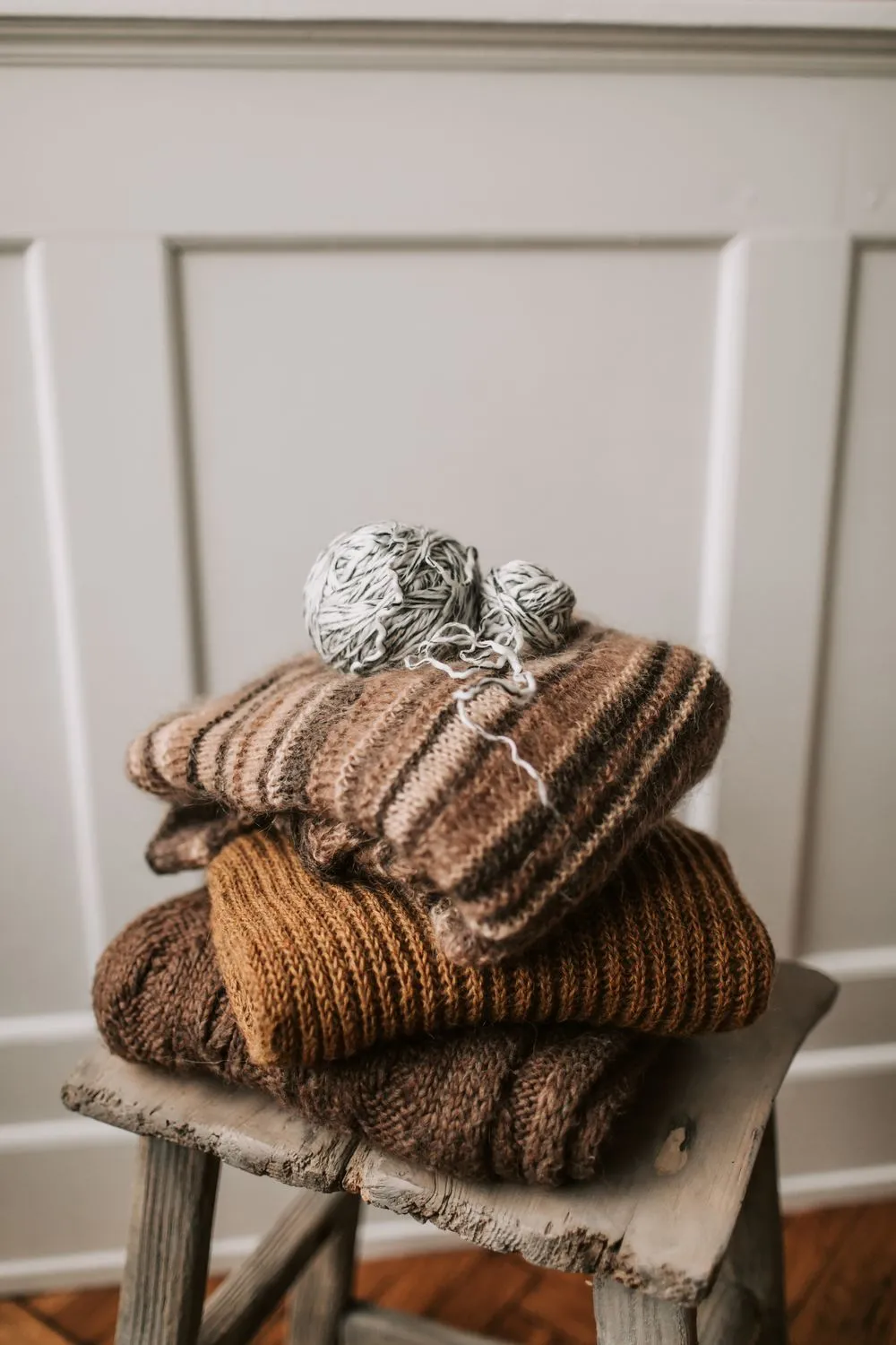 Folded merino wool knits stacked on a wooden stool beside a ball of natural yarn.