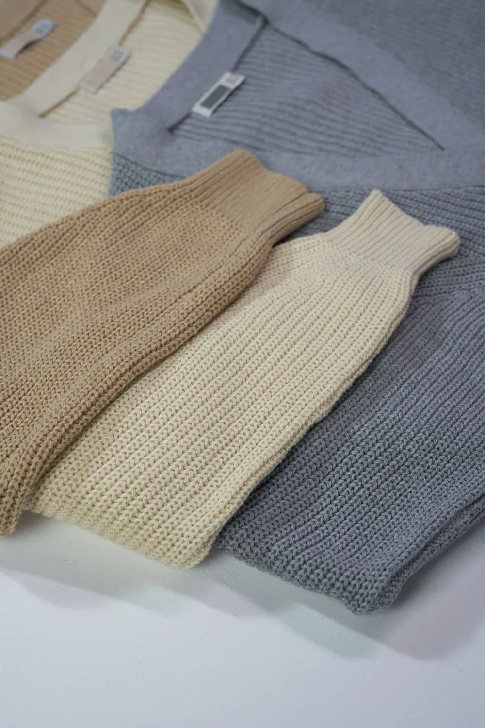Folded ribbed organic cotton cardigans in muted neutral shades.