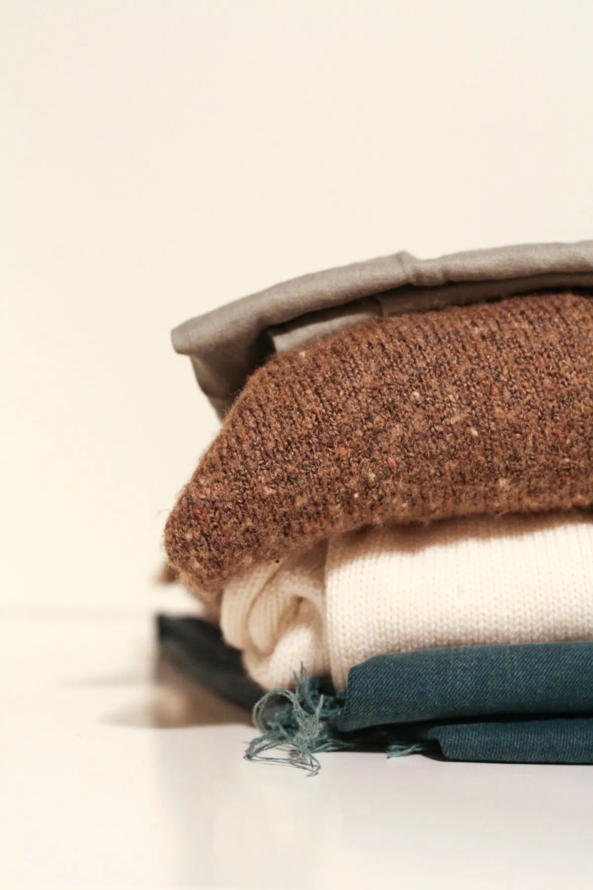 A folded stack of boxy crew sweatshirts in neutral bone and oatmeal tones.