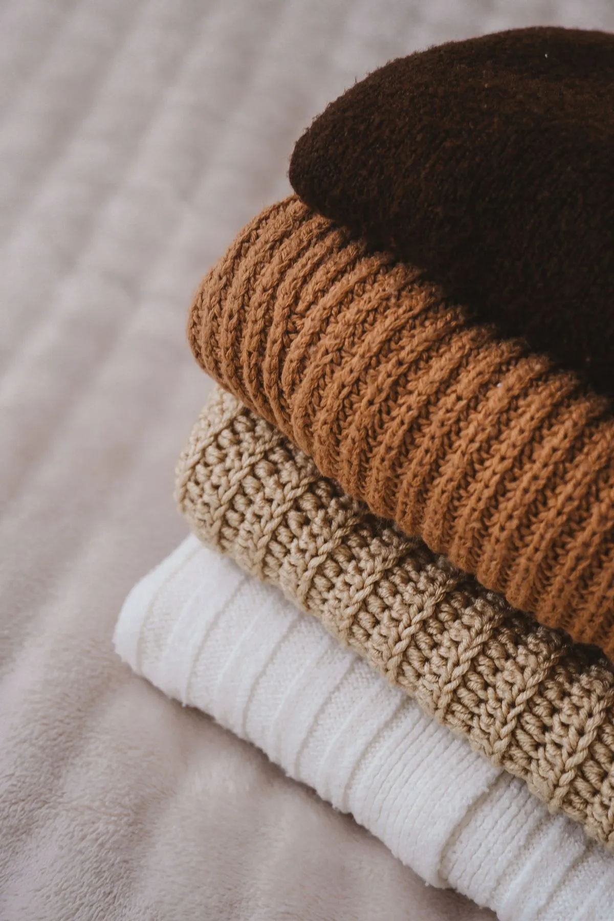 A warm folded stack of merino wool knit crews in soft camel and ecru.