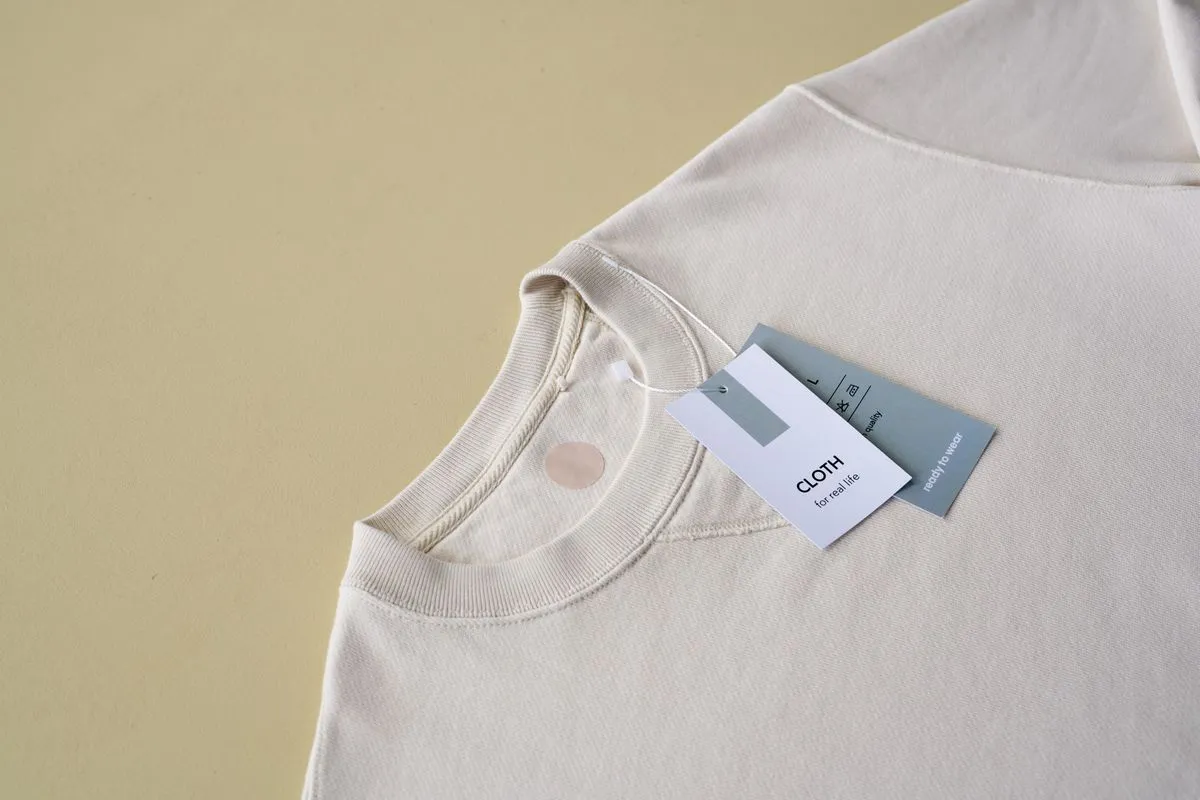 A cream organic cotton t-shirt, neatly folded with its paper hang tag visible.