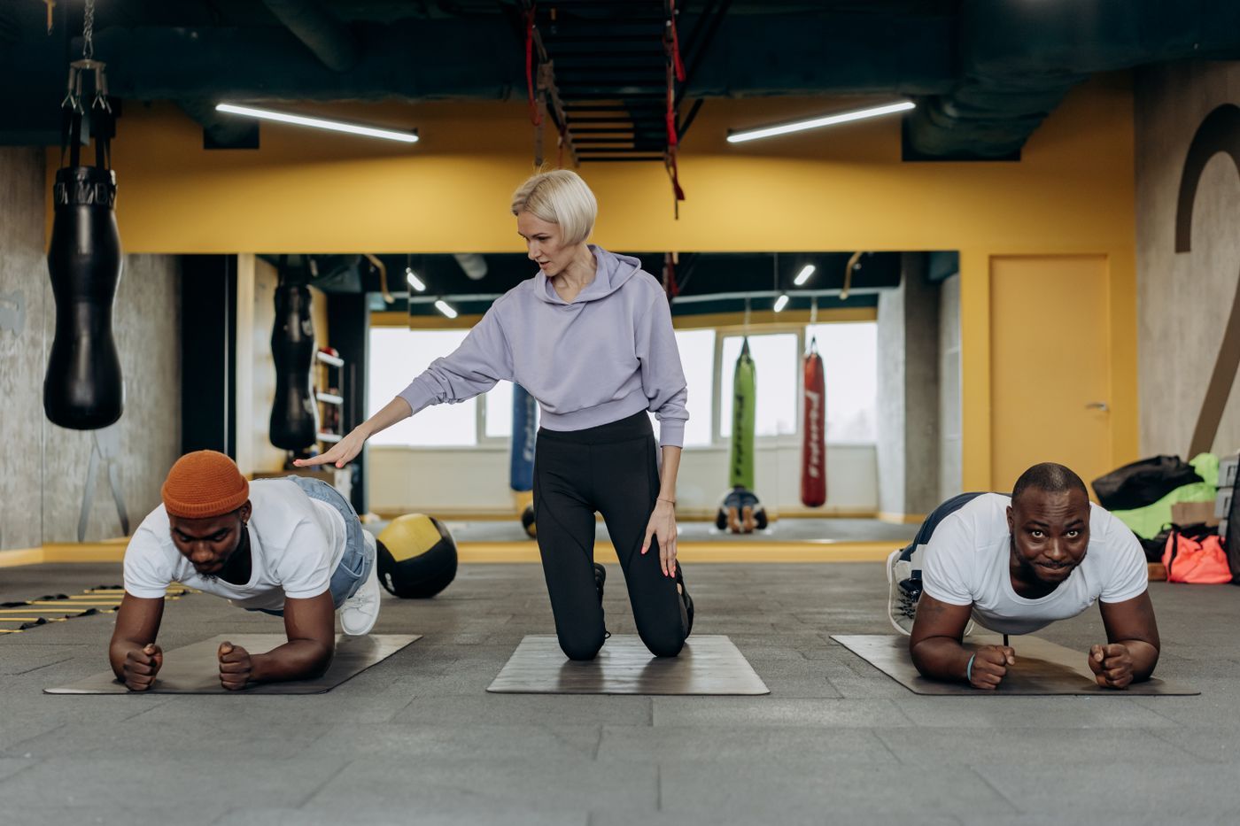 Female coach guiding two clients through planks on mats in a gym during a community training session