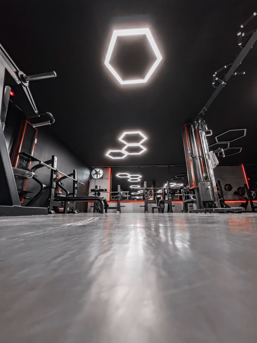 Sleek modern gym interior with hexagon LED lighting, racks and machines, dark walls with red accents