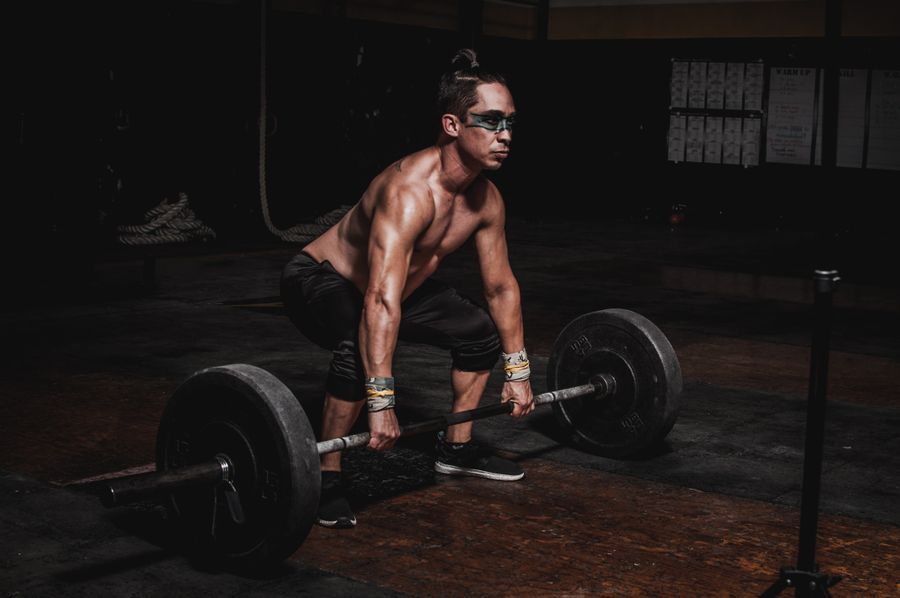 Muscular shirtless lifter set up at the bottom of a deadlift with a loaded barbell in a dark gym