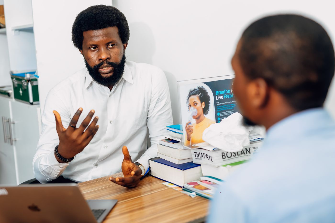 Practitioner in a clinic office gesturing as he reviews findings with a patient seated across a wooden desk, representing collaborative review of lab results.