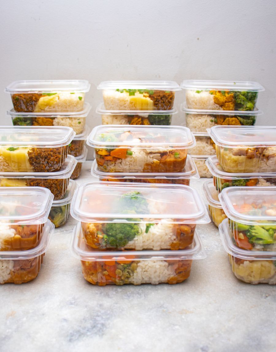 Stacked clear meal-prep containers filled with rice, broccoli, carrots and roasted vegetables, representing nutrition planning and whole-food meal support.