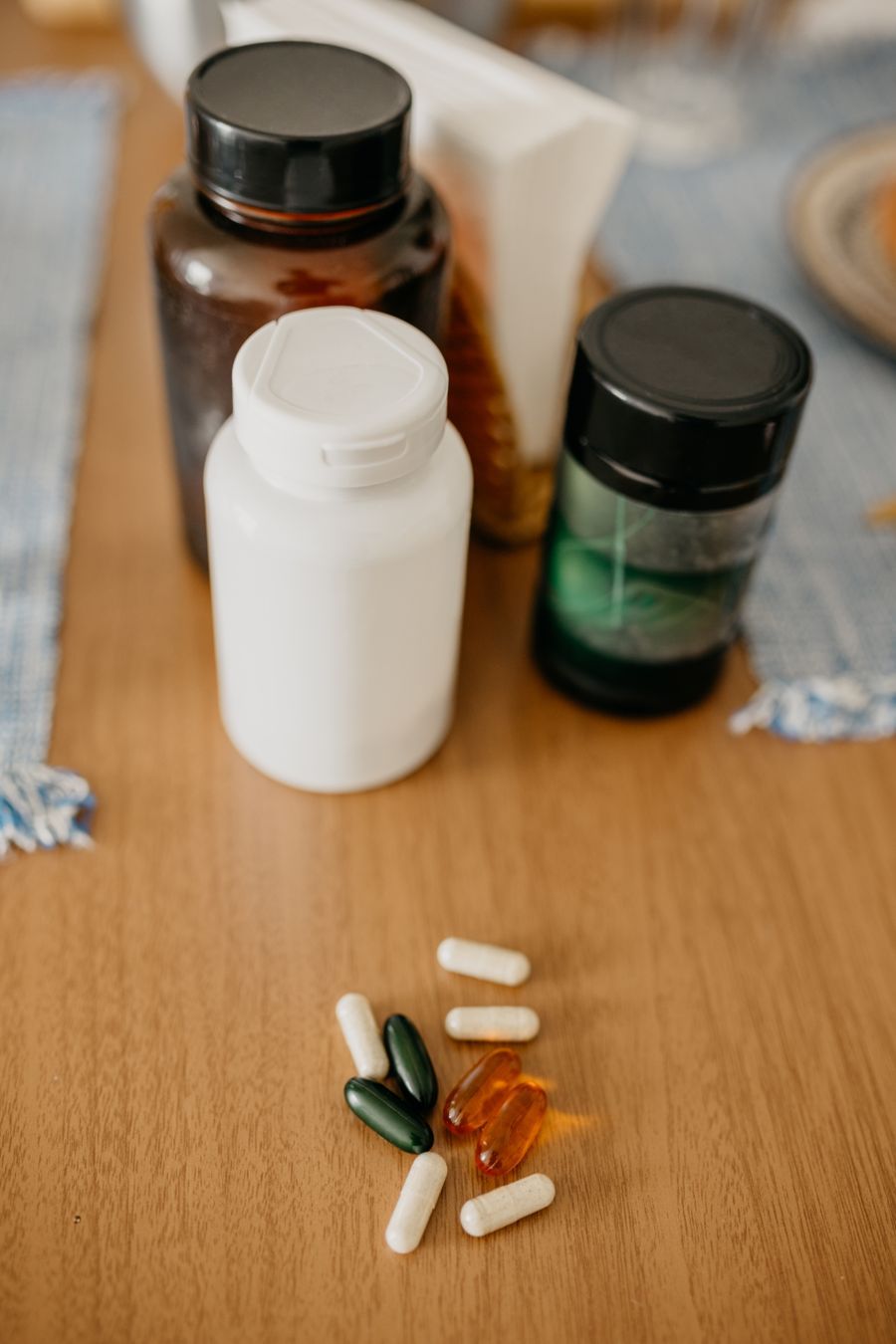 Amber and white supplement bottles with a scatter of capsules and softgels on a warm wooden table, representing targeted supplement protocols.