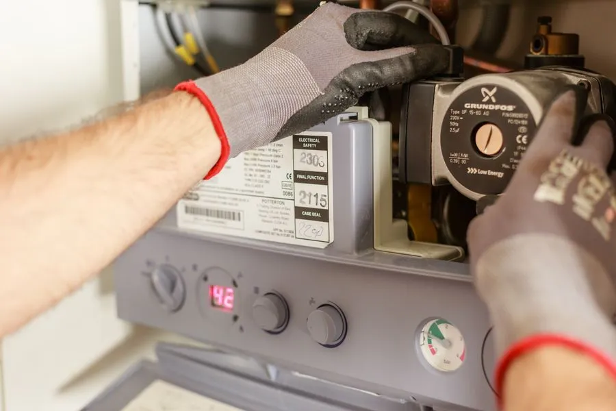 Technician's hands adjusting and servicing a home heating boiler system with instruments